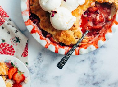 Top down view of a berry pie with a spoon and whipped topping.