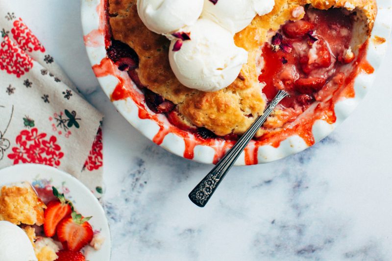 Top down view of a berry pie with a spoon and whipped topping.