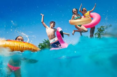 Young teenagers jumping into a lake with inner tubes.