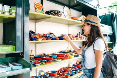 A woman with a hat and overalls shops at a street market.