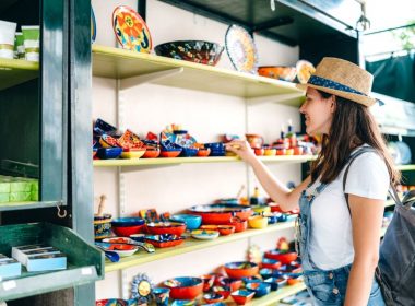 A woman with a hat and overalls shops at a street market.
