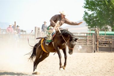 A man rides a horse during a rodeo with crowd surrounding the pen.