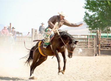 A man rides a horse during a rodeo with crowd surrounding the pen.