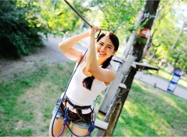 A young woman in a harness navigates a ropes course.