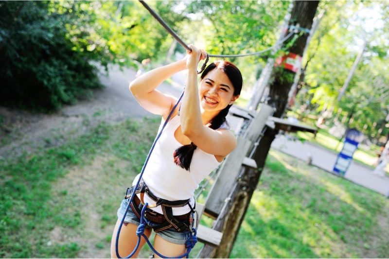 A young woman in a harness navigates a ropes course.