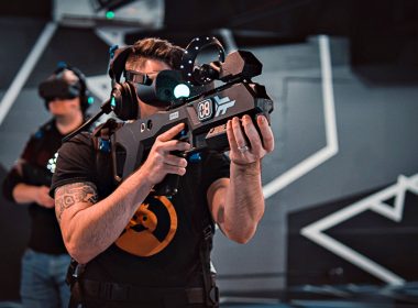 A man wears a virtual reality headset and holding a gaming gun in a Zero Latency gameroom.