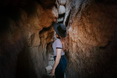 A woman walks into small tunnel in a rocky cave