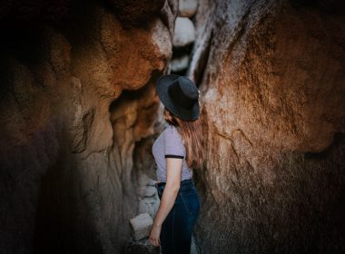 A woman walks into small tunnel in a rocky cave
