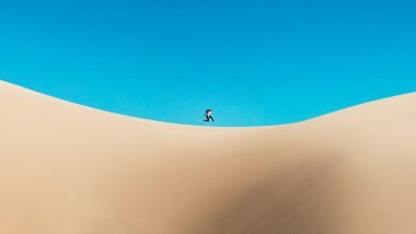 A person jumps at the top of a sand dune.