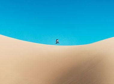 A person jumps at the top of a sand dune.
