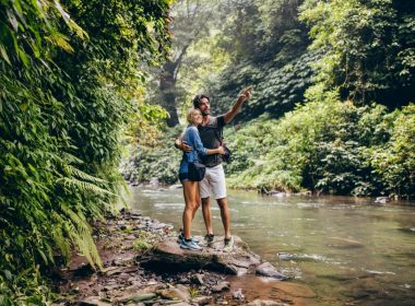 Two hikers standing on a rock in a creek pointing to a natural beauty.