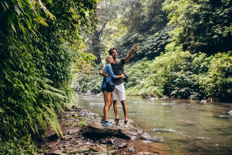Two hikers standing on a rock in a creek pointing to a natural beauty.