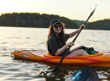 A happy, smiling woman kayaks with her friends on a lake at sunset.