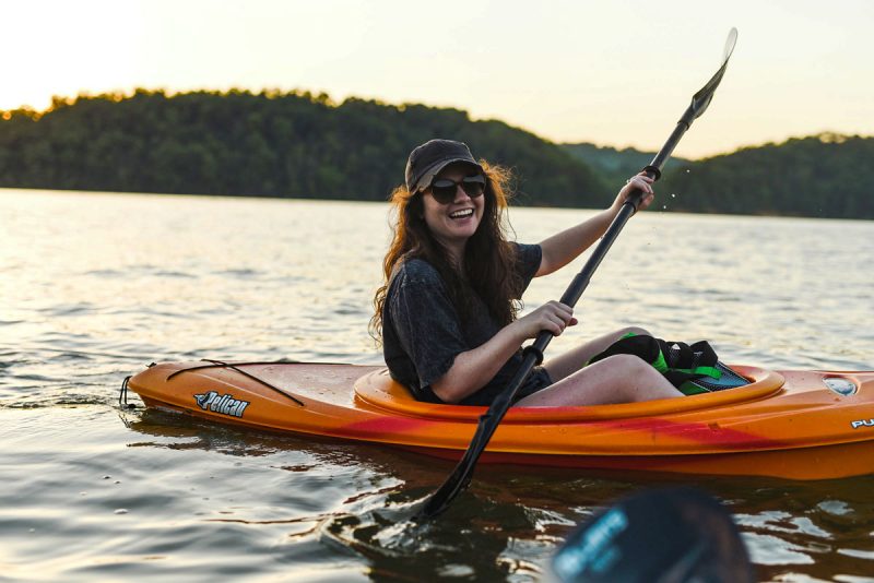 A happy, smiling woman kayaks with her friends on a lake at sunset.