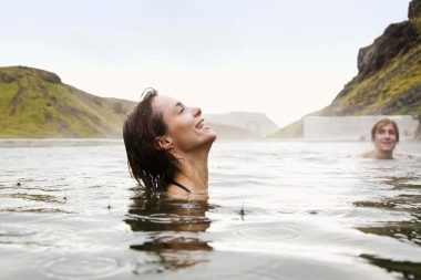 A woman smiles as she enjoys a hot spring outside and it starts to rain.