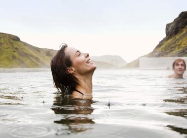 A woman smiles as she enjoys a hot spring outside and it starts to rain.