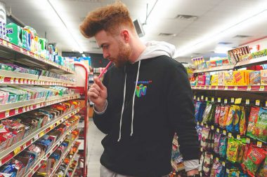 A man eating candy as he peruses the candy aisle in a gas station.