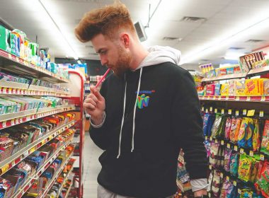 A man eating candy as he peruses the candy aisle in a gas station.