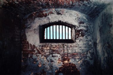 Inside a deteriorated brick prison looking out the barred window.