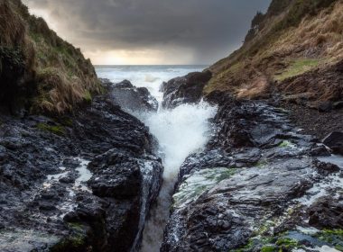Looking down the crevice cut through the Earth at Devil's Churn as waves crash against rock.