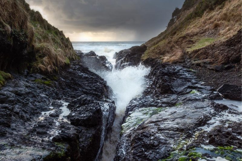 Looking down the crevice cut through the Earth at Devil's Churn as waves crash against rock.