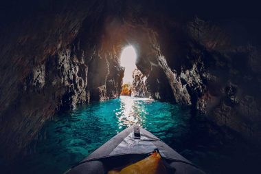 A kayaker paddles through a rocky cove over clear jewel-toned waters.