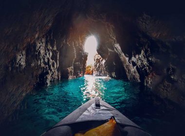 A kayaker paddles through a rocky cove over clear jewel-toned waters.
