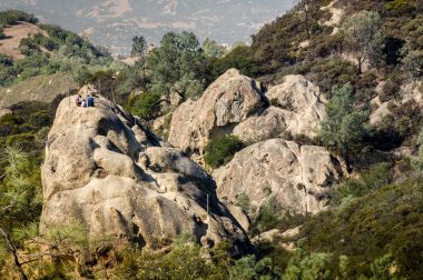 Hikers sit high up on a boulder in Rock City, California.