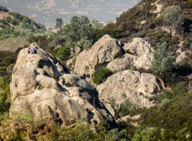 Hikers sit high up on a boulder in Rock City, California.