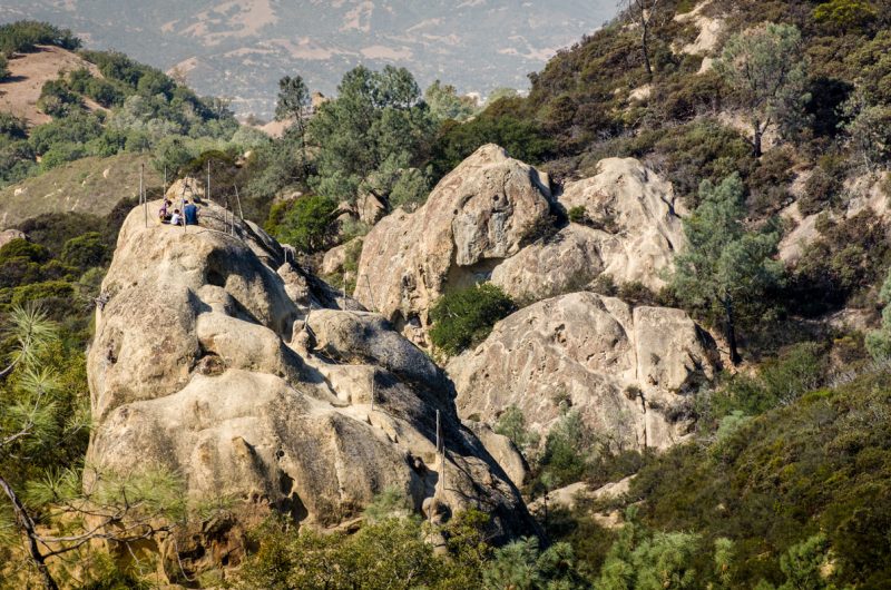 Hikers sit high up on a boulder in Rock City, California.