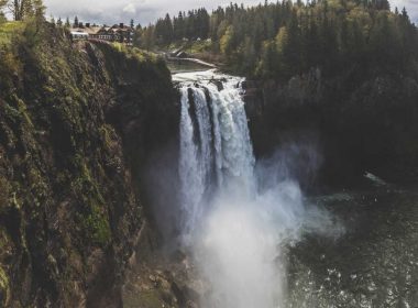 Snoqualmie Falls in Washington thunders over a cliff with houses just up river.