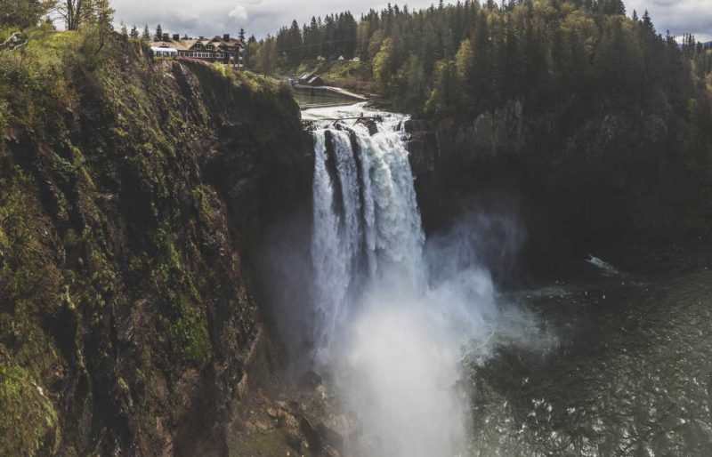 Snoqualmie Falls in Washington thunders over a cliff with houses just up river.