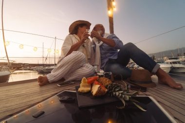 A couple of baby boomers toast with champagne while sitting on the deck of a sailboat at sunset.