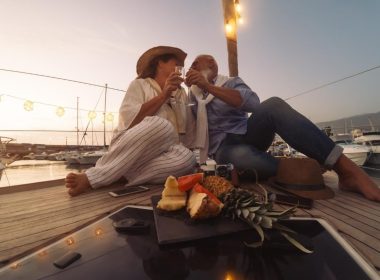 A couple of baby boomers toast with champagne while sitting on the deck of a sailboat at sunset.