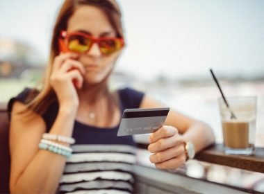 A woman on the phone holding up her credit card while on vacation.