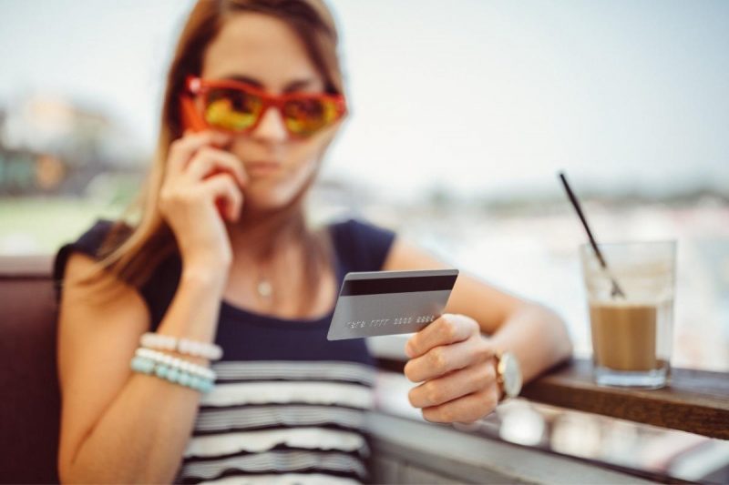 A woman on the phone holding up her credit card while on vacation.