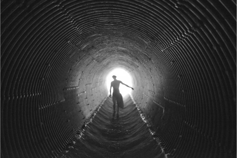 A silhoutte of a man walking down a ridged culvert tube below a road.