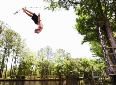 A man back flips off a rope swing into a water.