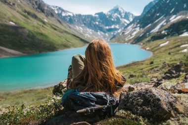 A woman sits and enjoys the view of a turquoise river and mountains in Alaska on a summer day.