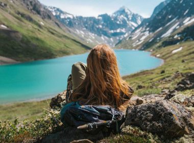 A woman sits and enjoys the view of a turquoise river and mountains in Alaska on a summer day.