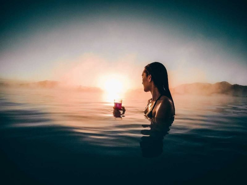 A woman holds a drink in the hot spool at sunrise.