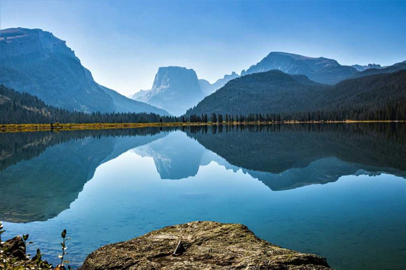 A glassy Green River reflecting the sky and mountain landscape in Wyoming.