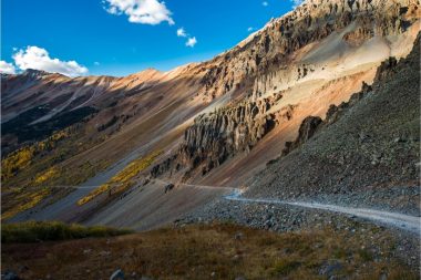 A skinny dirt road winds along a mountains side towards the abandoned town of Ophir, Utah.