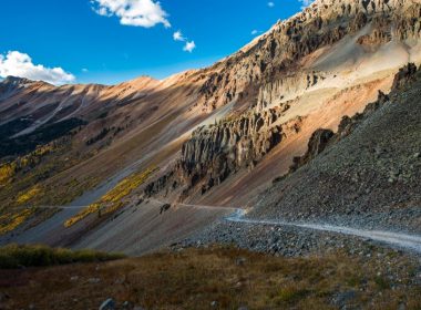 A skinny dirt road winds along a mountains side towards the abandoned town of Ophir, Utah.