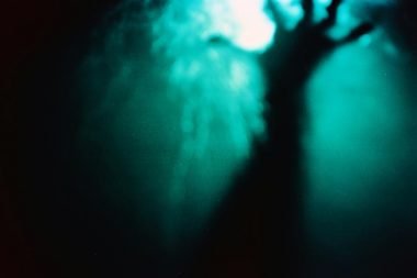 The dark form of a blurry hand under dark water reaching towards the light at the surface of the water.