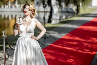 Portrait of a beautiful woman in white dress as a well-known actress holding famous movie award on the red carpet outdoors