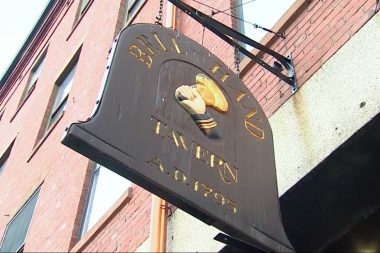 A brown wooden sign hanging outside Bell In Hand Tavern in Boston.