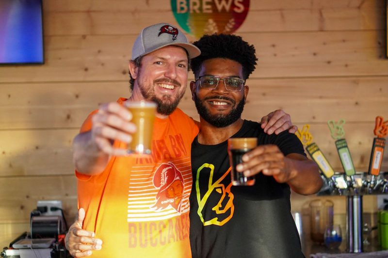 Two bros holding up craft beers and smiling in a brewery.
