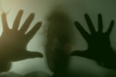 A blurry figure through a dark see through glass window.