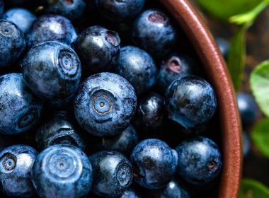 Close up of a wooden bowl of freshly washed blueberries.